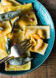 a blue bowl filled with ravioli and spinach covered in sauce, topped with a fork