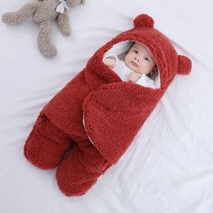 a baby in a red bear costume laying next to a teddy bear