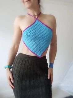 a woman wearing a blue and pink crochet top with her hands on her hips