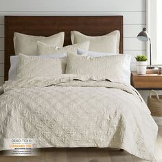 a bed with white linens and pillows in a room next to a lamp on a wooden headboard