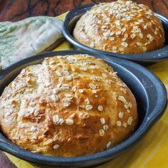 two loafs of bread sitting in black pans on top of a wooden table