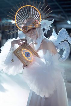 a woman dressed in white and holding a clock with angel wings on her head while standing next to a building