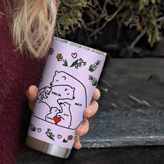 a woman holding a pink tumbler with a drawing of a bear and heart on it