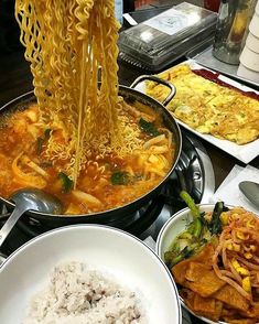 noodles being cooked in a wok on top of a stove with other dishes and utensils