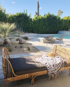 a bench with a blanket on it in front of a swimming pool and cactus trees