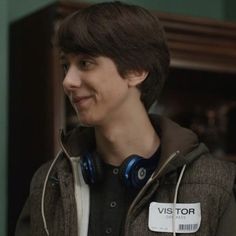 a young man with headphones and a name tag on his jacket is smiling at the camera