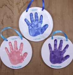 three handprinted ornaments hanging on a wooden table with blue and pink ribbons around them