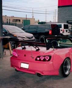 a pink sports car parked next to other cars in a parking lot with the hood up