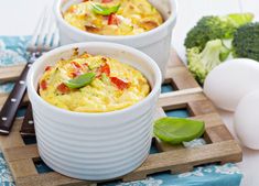 two white bowls filled with food sitting on top of a wooden cutting board next to eggs and broccoli