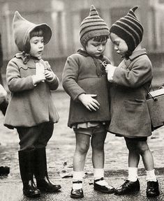 three little kids standing next to each other in the rain, wearing hats and coats