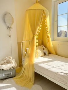 a yellow canopy bed in a bedroom with white sheets and pillows on the floor next to a window