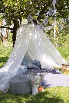 a white tent is set up in the grass under a tree with flowers on it