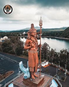 a statue of a woman holding a spear on top of a building next to a body of water