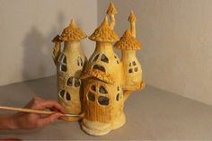 a person holding a wooden stick near a clay model of a house with windows and turrets