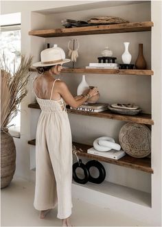 a woman in a white dress and hat is arranging items on wooden shelvings