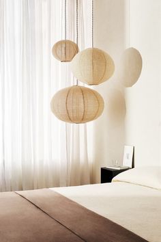 three lamps hanging from the ceiling above a bed in a room with white walls and curtains