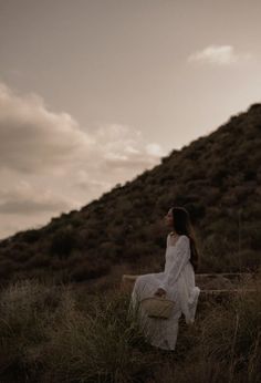 a woman is sitting on a bench in the grass and looking up into the sky