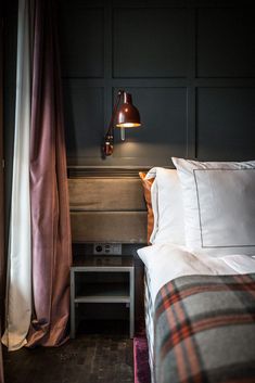 a bed with two pillows and a lamp on the headboard in a room that has dark wood paneling