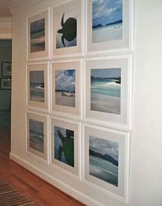 a wall with many pictures on it in a room that has wood floors and white walls