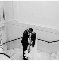 a bride and groom kissing on the stairs at their wedding reception in black and white