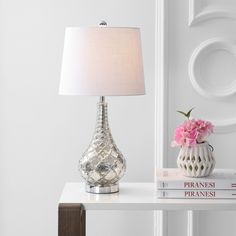 a table with a lamp and books on it next to a white vase filled with pink flowers