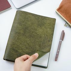 a person is holding a pen and looking at a book on a table with other items