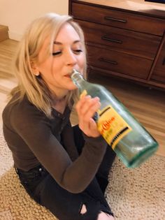 a woman sitting on the floor drinking from a bottle