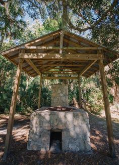 an outdoor stone oven in the middle of some trees and grass with a canopy over it