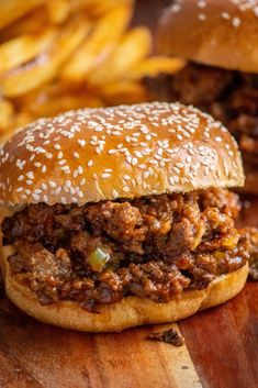 a sloppy joe sandwich with french fries in the background on a cutting board, ready to be eaten