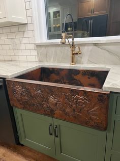 a large copper sink in a kitchen with green cabinets