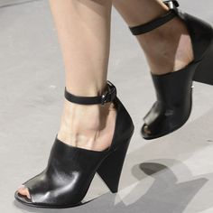 a woman's feet wearing high heeled black shoes with ankle strap and buckles