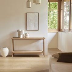 a white vase sitting on top of a wooden table in a living room next to a window