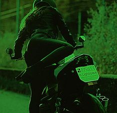 a person riding on the back of a motorcycle in the dark with green light behind them