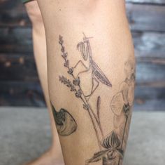 a woman's leg with a tattoo on it that has an image of a praying mantisbee and flowers