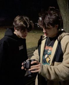 two young men standing next to each other while looking at a cell phone in front of them