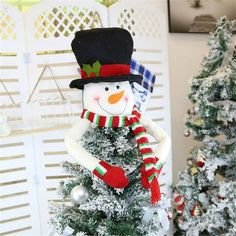 a snowman sitting on top of a tree next to a white christmas tree with red and green decorations