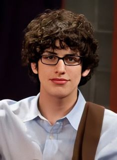 a young man with glasses and suspenders is looking at the camera while holding his hand up