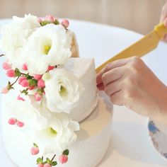 a person cutting a cake with a yellow knife and flowers on it's side