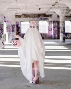 a woman in a white ghost costume holding a pink ball and a jack - o - lantern