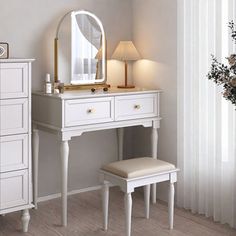 a white dressing table with a mirror and stool next to a flower vase on the floor