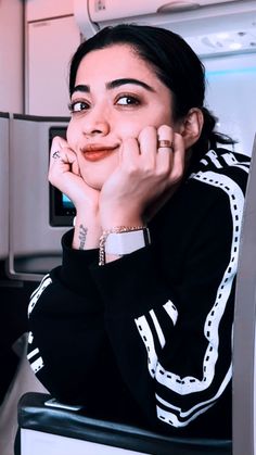 a woman sitting on an airplane seat with her hand under her chin and looking at the camera