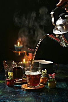 tea being poured into a glass cup on top of a table with other cups and saucers