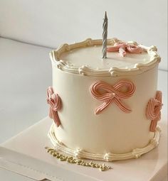 a white cake with pink bows and a single candle