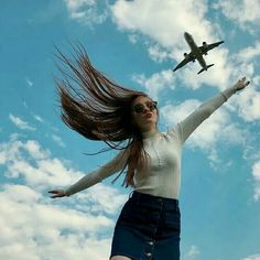 a woman with her hair in the air and an airplane flying overhead behind her on a sunny day