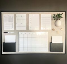 a white board with black and white papers on it next to a potted plant