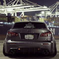 the back end of a silver car parked in front of a large container ship at night