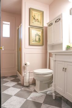 a white toilet sitting in a bathroom next to a sink and cabinet with pictures on the wall