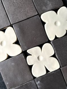 four white flowers on black and gray tiles with one flower in the middle, two are shaped like hearts