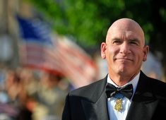 a bald man in a tuxedo with an american flag on the back ground