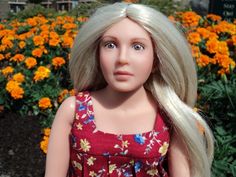 a doll with blonde hair standing in front of flowers